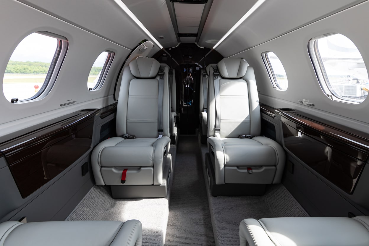 Interior de cabine executiva do Embraer Phenom 300E, poltronas de couro claro.